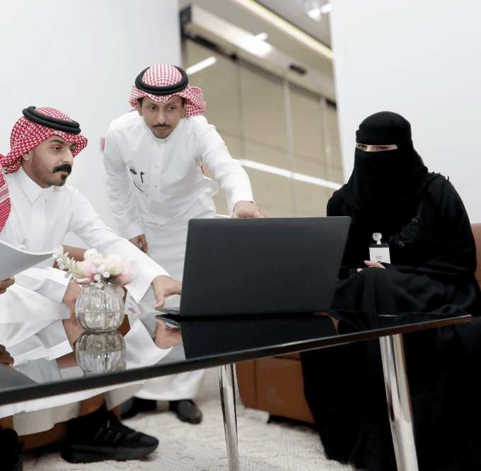 امرأة ورجلان يناقشان شيئاً ما أثناء النظر إلى شاشة كمبيوتر محمول.